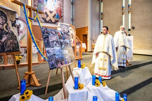 Fr. Yevhen Zadorozhnyi refering his homily to the display featuring pictures of the Ukraine war